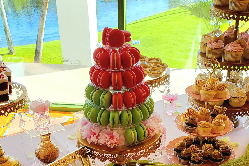 Dessert table with various treats including cookies, fruit towers, and cupcakes outdoors.