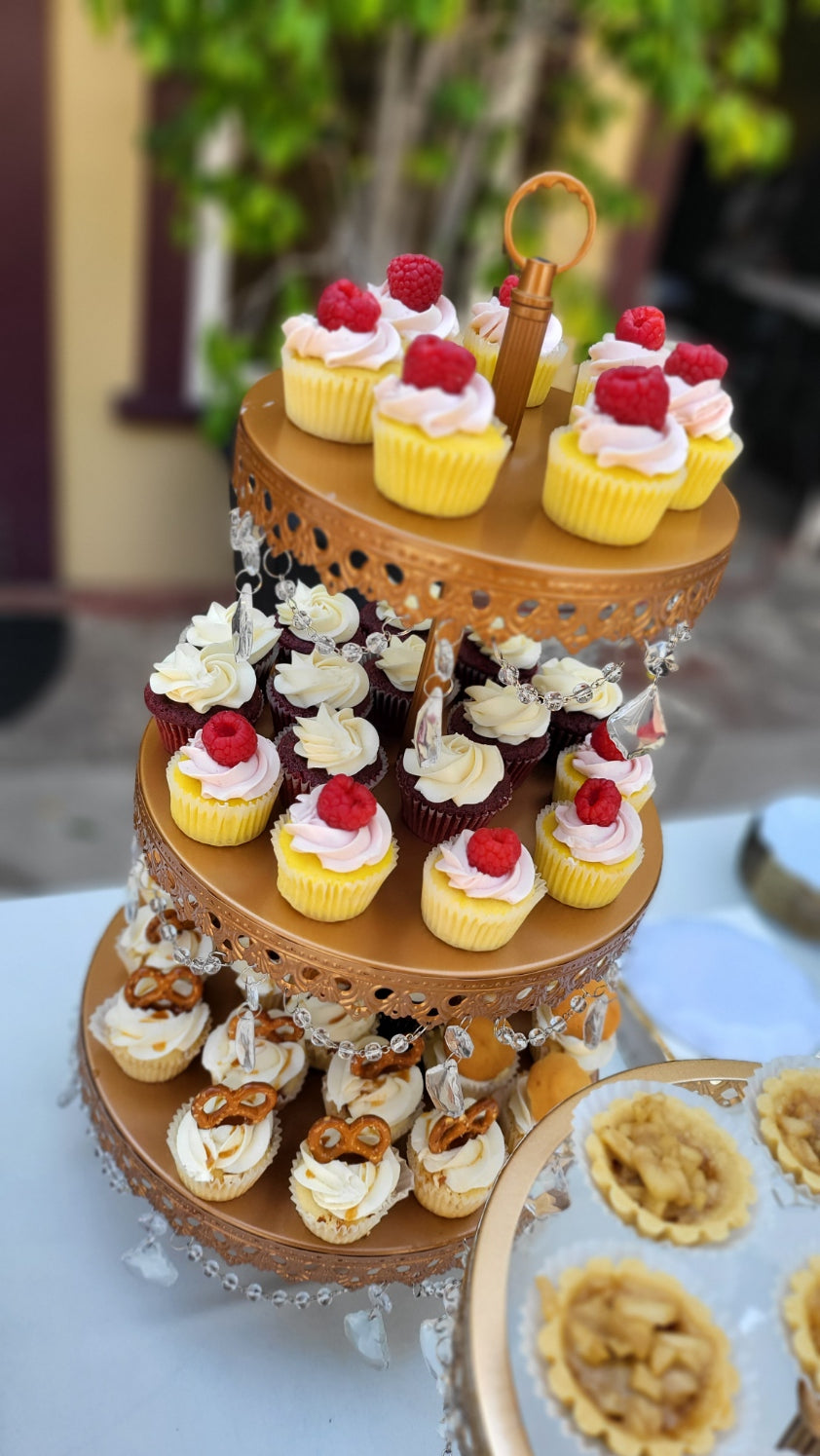 Close up picture of a 3 tiered cupcake tower on a wedding dessert table outside.
